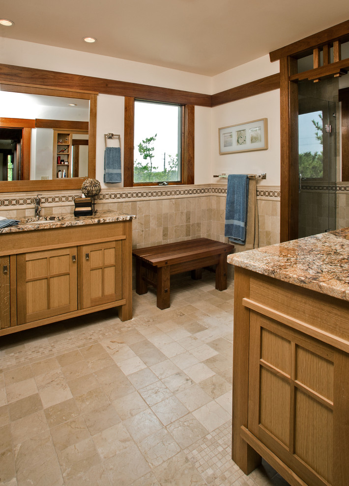 craftsman bathroom with brown tiles, brown wooden cabinet with brown marmer counter top, dark brown long low chair, brown tile wainscoting, brown framed window and door 