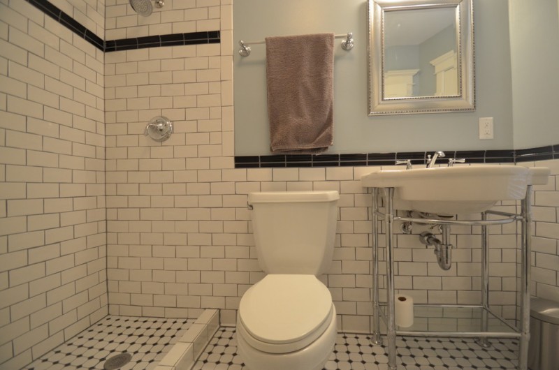 craftsman bathroom with white small tiles in flooring, white tiles in walls in the shower area, wainscoting in toilte and wastafel area, white toilet, white wastafel 
