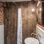 small bathroom with white tiles half down and orange tiles half top wall, one brwon tiles side wall, golden shower head, white curtain, white sink, golden faucet, wood vanities,