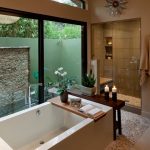 Small Rock Tiles Flooring Idea Rectangular Bathtub With Wooden Panel Walk In Shower Space With Beige Ceramic Tiles Walls And Small Rock Tiles Floors Shower Bench Recessed Shelves