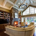 vaulted living room with brown ceiling and walls, brown sofa, dark wooden shelves, stone fire place, chandelier