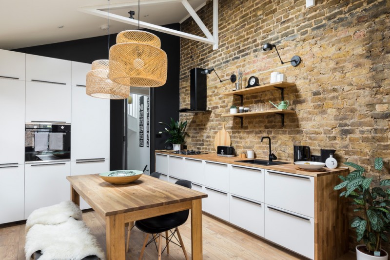 industrial kitchen with industrial shelving unit red brick walls wood countertop wood dining table with modern black chairs medium toned wood floors without finishing white recessed cabinets