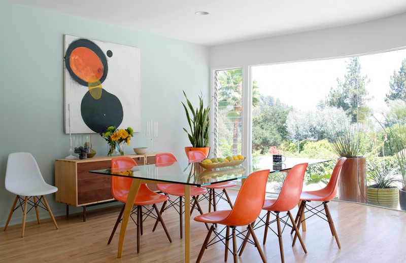 midcentury dining set with glass top table with wooden legs, orange sleek chairs with wooden legs and black steel support under the seating