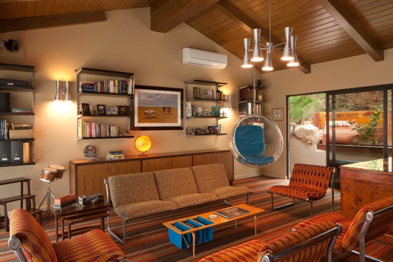 living room with orange patterned chairs, warm brown sofa, wooden long coffee table, nesting side table, glass hanging bulb chair with blue cushion, wall shelves
