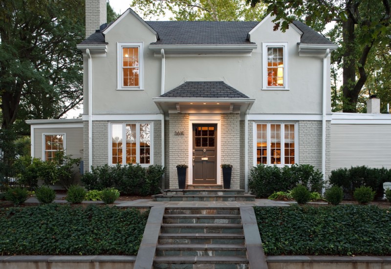 classic gray exterior home with evergreen shrubs stairs pathway brick wall gray wall glass windows in white trim gray front door and roofs