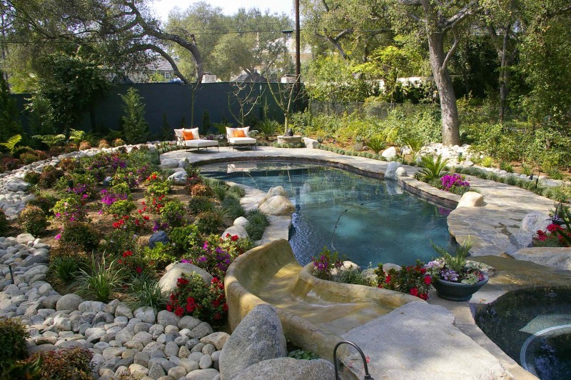 hot tub water feature colorful flowers boulders stone paving pebble outdoor seating waterfall