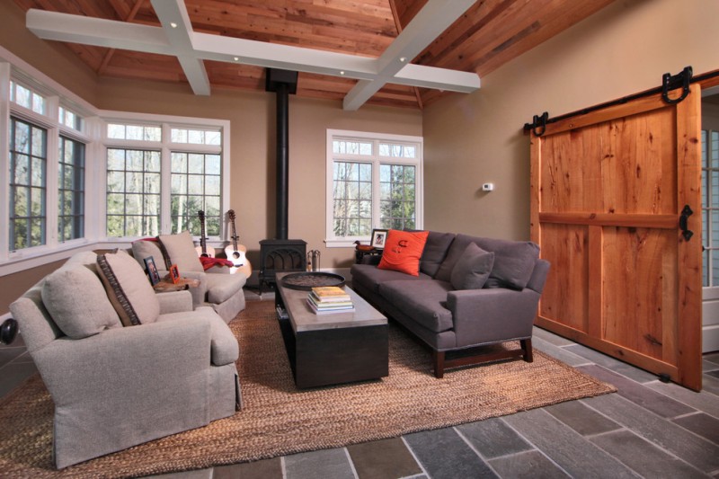 tan living room grey couch grey armchairs coffee table area rug tan walls open ceiling big barn door grey floor tiles windows