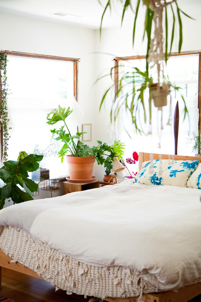 70s bedroom white duvet wooden bed colorful pillows indoor plants white wall wooden side table windows wooden floor