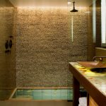 Bathroom With Grey Flooring, Stones Wall In The Shower Area, Wooden Cabinet With Marble Top