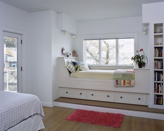 built in bed near the window sill with white wooden bedding, white cushion, colorful pillows, storage under, bookshelves ath the foot of the bed
