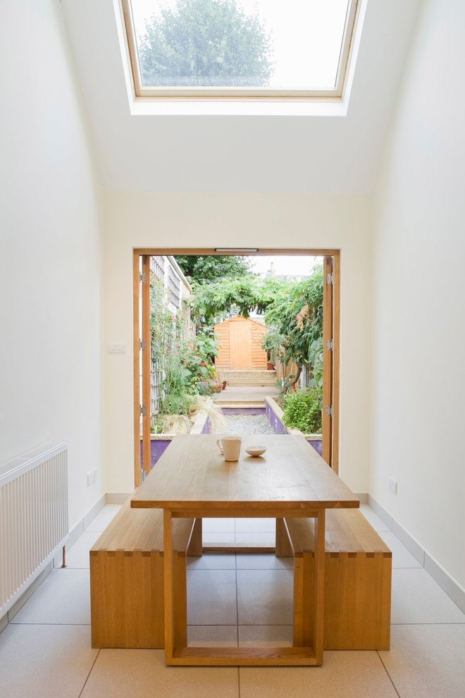narrow dining room with white floor, white painted wall, glass roof, open garden on one side, a square table with two benches