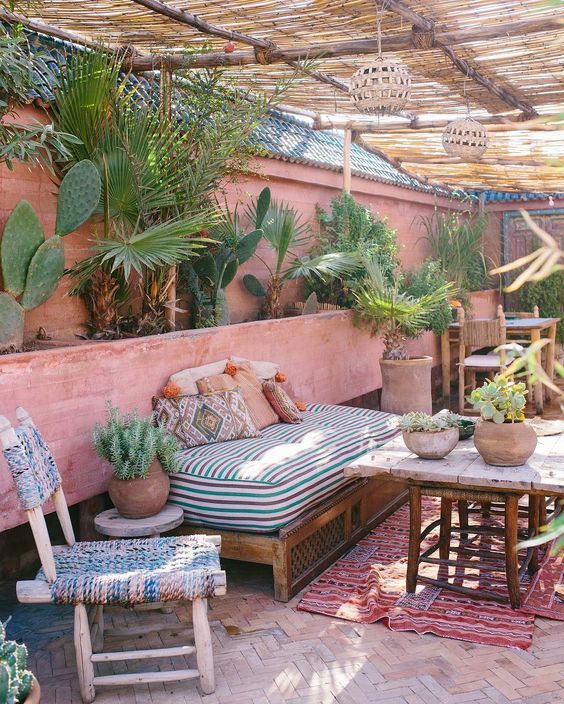 patio with pink wall, wooden bench with colourful cushion, wooden coffee table wih white top, plants, rattan ceiling