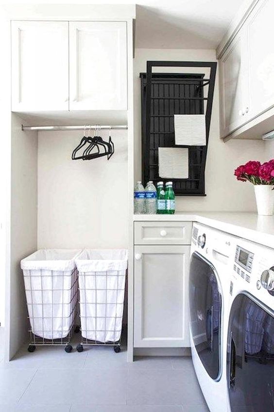 small laundry room with white wall, white tile, two machines, cabinets, white marble top, drying racks, hangers, laundry baskets
