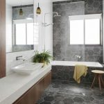 Bathroom With Hexagonal Grey Tiles On Teh Wall, Floor, And Tub With White Inside, White Vanity Top, Wooden Cabinet, Large Mirror
