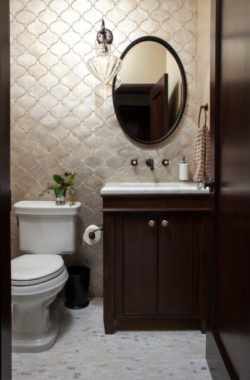bathroom with marble floor, white toilet, wooden cabinet with white marble vanity, round mirror, sconce, pearl colored arabesque tiles