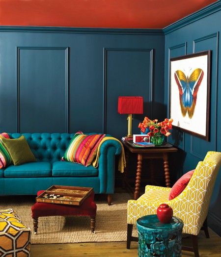 chesterfield sofa in teal with tufted back in a living room with teal orange wall, wooden side table, yellow chair, yellow ottoman