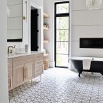 Bathroom, Patterned Floor Tiles, White Wall, Wooden Vanity With White Top, Large Mirror, Wooden Floating Shelves, Black Tub, Chandelier