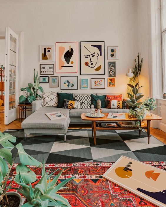bohemian living room, wooden floor, geometric grey rug, grey sofa, wooden table, colorful pillows, white wall, wall decorations, orange rug, plants