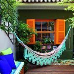 Hammock With Green Big Fringe, Wooden Floor, Green Wall, Orange Window, Olorful Cushion On Wooden Bench