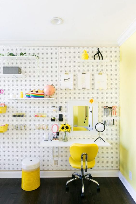 make up stationwith white pegboard wall, dark wooden floor, white floating table, yellow office chair