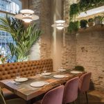 Wooden Dining Table, Pink Velvet Chairs, Green Velvet Chair, Brown Leather Bench, White Open Brick Wall, Plants On The Wall Windows, Pendants