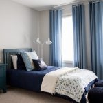 Blue And Gray Bedroom Gray Walls Blue Bedding Blue Wooden Headboard White Standing Lamp Blue Curtains Windows Round Wall Mirror Black Ottoman Nightstand