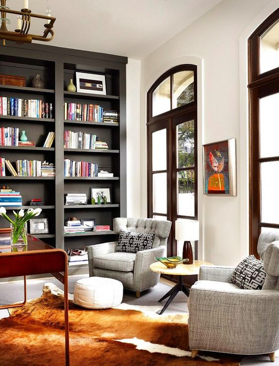 dark tall bookcase, grey chairs, white wall, tall windows brown wooden framed, beige floor, rug, round coffee table