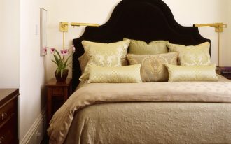 very narrow bedside table black headboard wooden dresser gold wall sconces silk pillows beige beding grey rug white walls drawer