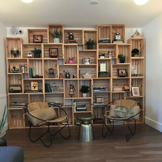 wooden crates stack tidily to the wall with books, decorations, plants, wooden floor, round chair with leather seating, metal coffee table