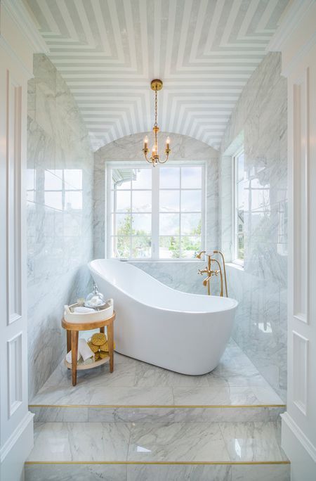 bathroom, white marble ont he floor, wall, patterned ceiling, chandelier, white tub, golden faucet, wooden stol