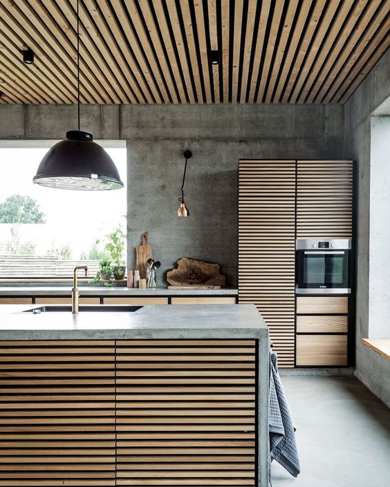 kitchen, seamless grey floor and wall, wooden slats island with grey top, wooden cabinet with grey top, wooden slats pantry, wooden slats ceiling, black pendant, golden sconces