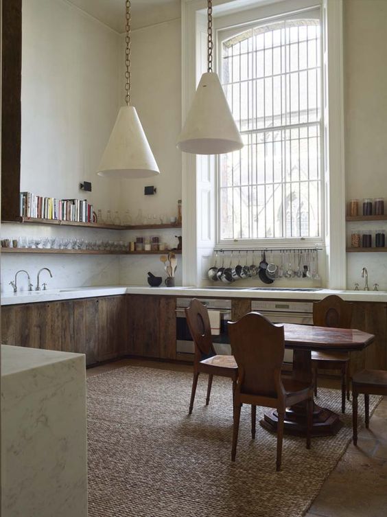 kitchen, wooden floor, rattan rug, white wall, wooden bottom cabinet with white top, white wall, wooden floating shelves, white pendants, wooden dining set