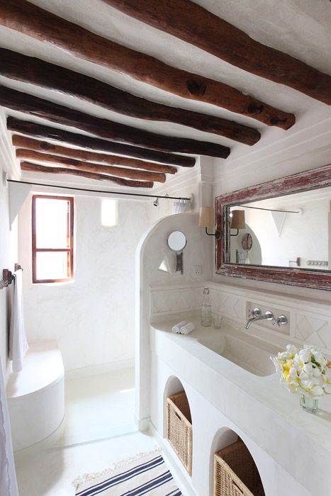 greek bathroom, whtie plastered wall and floor, white ceiling with wooden beams, white built in vanity and sink, rattan basket