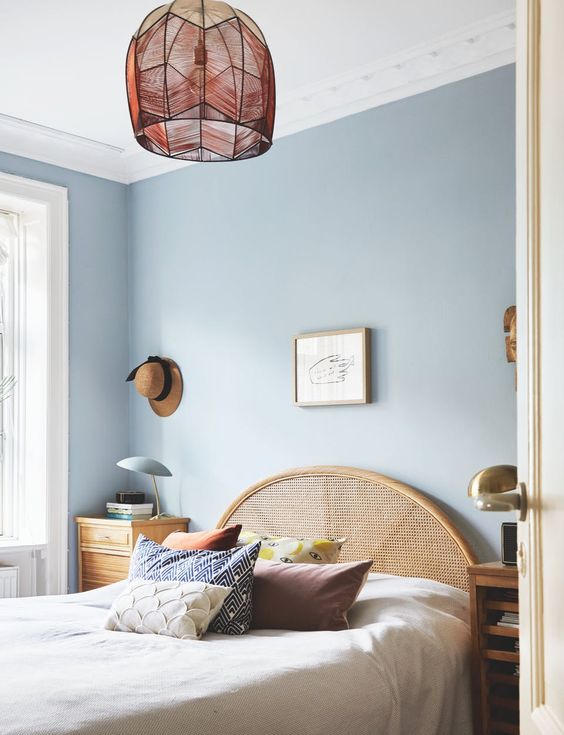 rattan headboard, white bedding, blue wall, pendant, wooden side table, wooden side cabinet