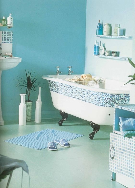 white tub with blue mosaic tiles on the rim, black claw foot, blue floor and wall, floating shelves, white sink