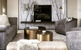 living room, whtie hexagonal floor tiles, beige wall, marble wall decoration, floating black shelves with TV, grey sofa, grey chairs, white bench, gold round coffee table