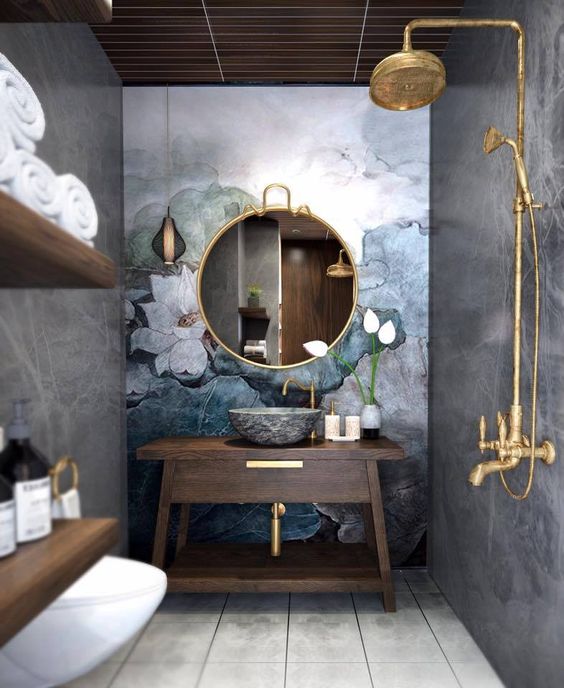 bathroom, grey wall, flower accent wall, golden round framed mirror, golden shower faucet, dark wooden vanity, wooden floating shelves