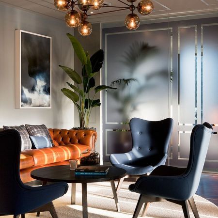 orange sofa with rufted back, navy chairs, black round coffee table, cream wall, brown glass chandelier