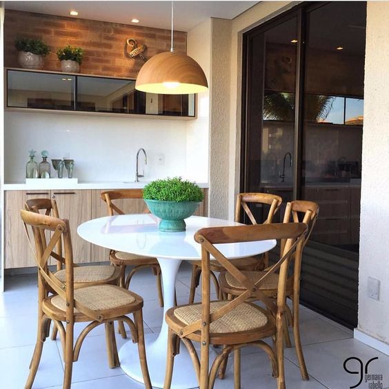 patio, white floor tiles, white wall, wooden vanity with white counter top, white round tulip table, wooden chairs with rattan seating, wooden pendant, black glass wall