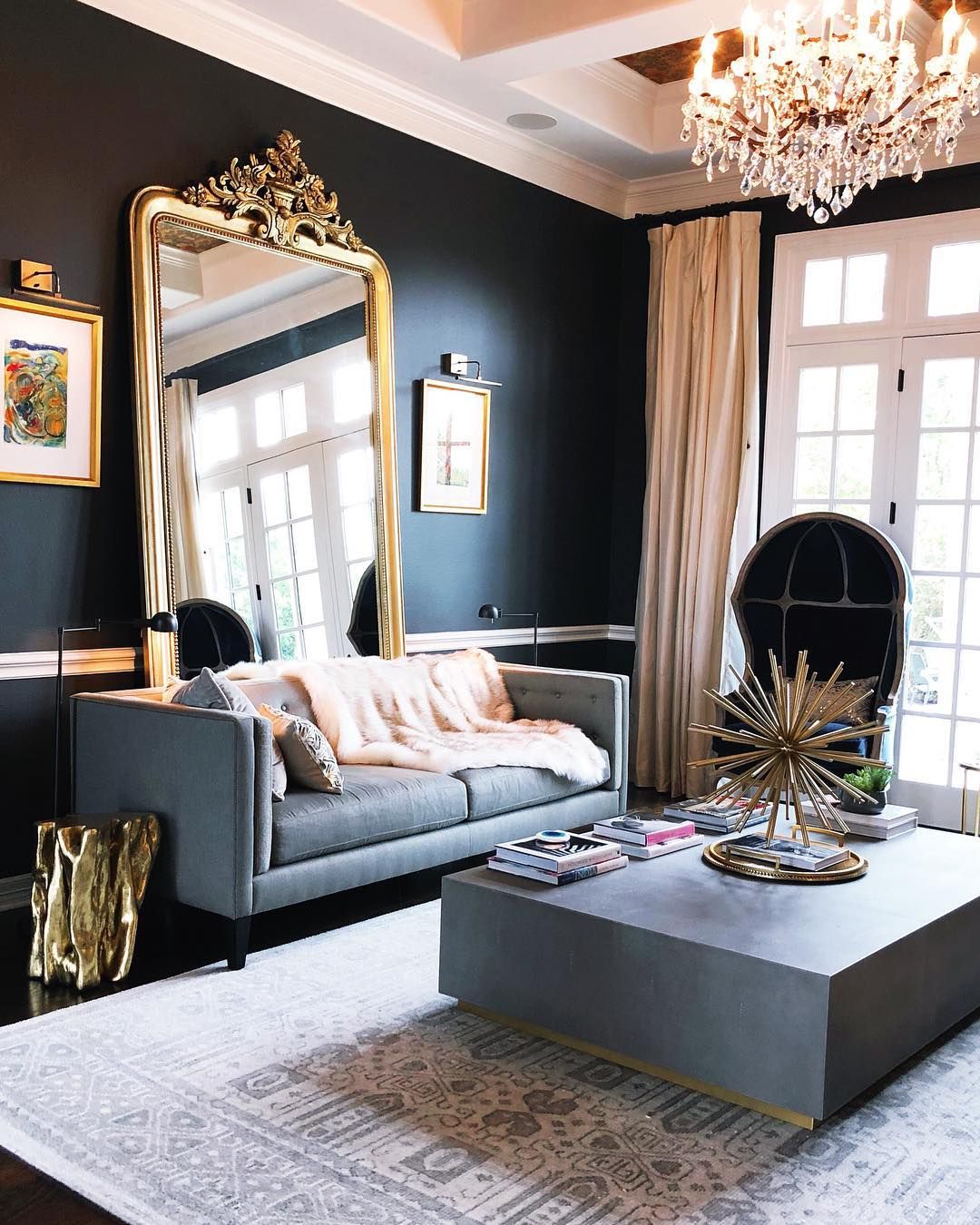 living room, black floor, grey rug, black wall, grey sofa, grey square coffee table, crystal chandelier, black round chair, golden framed mirror