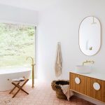 Bathroom, Orange Patterned Floor, White Wall, Wooden Floating Cabinet With White Top, White Round Sink, Ovale Mirror, White Tub, Golden Faucet