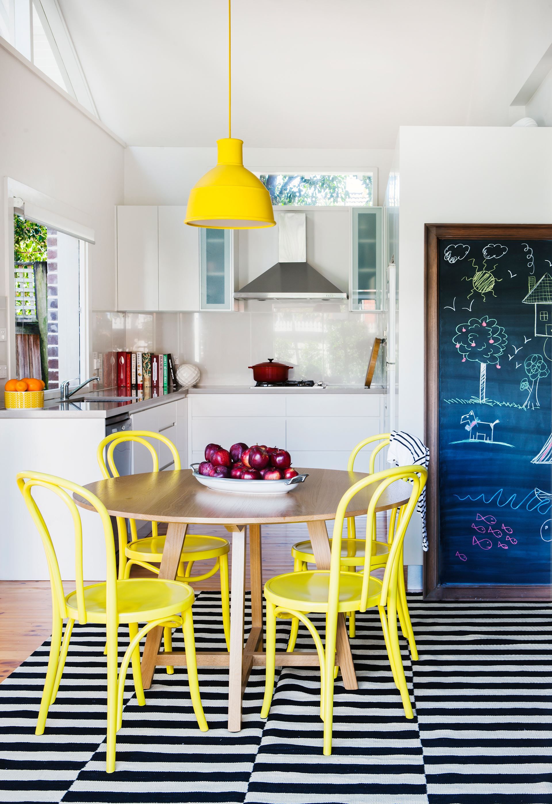 dining room, woode floor, black white striped rug, white kitchen cabinet, white wall, round table, yellow chairs, yellow pendant