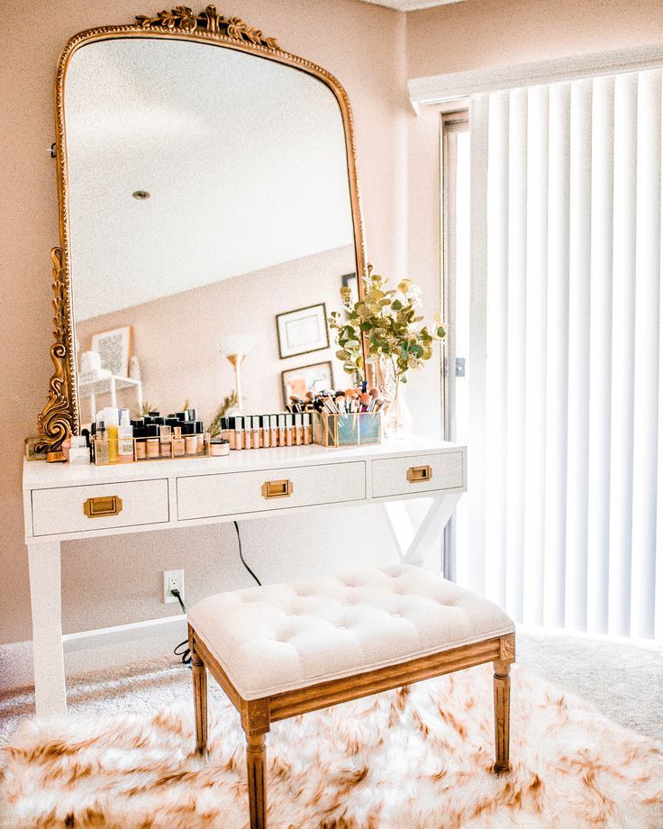 white wooden desk, white floor, white pink rug, golden stool with white cushion, golden framed mirror