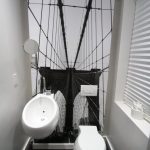 Half Bathroom With White Toilet, White Wall Mounted Sink, Dark Flooring, White Walls, Black And White Picture Of Bridges In The Back