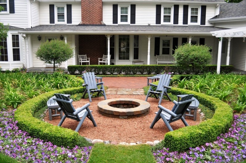 patio with round hedges and fire pit in th middle surrounded with grey chairs and bench