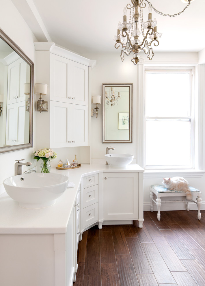 white bathroom with white wall and ceiling, white vanity, chandelier, wooden flooring, mirror, sconces