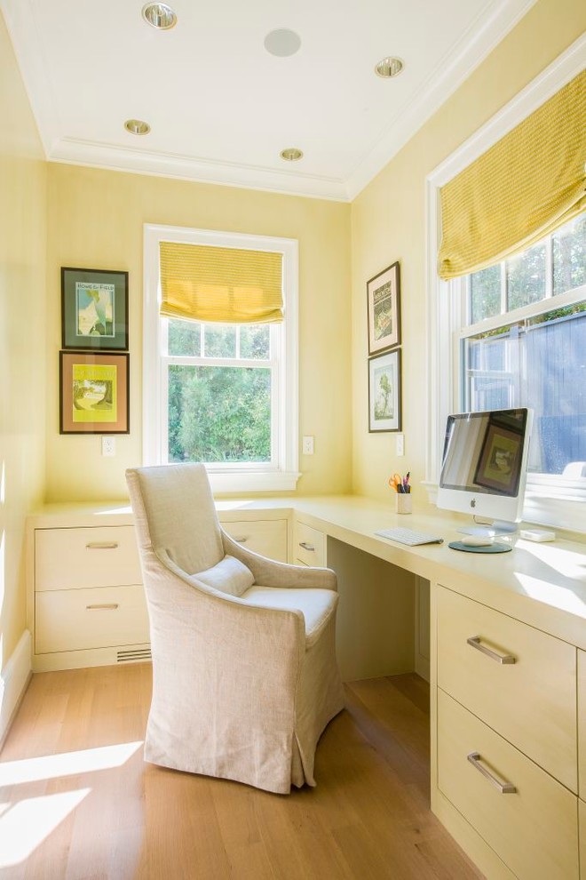 cozy and warm study room with L shape built in computer desk white chair slipcover light toned hardwood floors light yellow walls accented by bright yellow window curtains