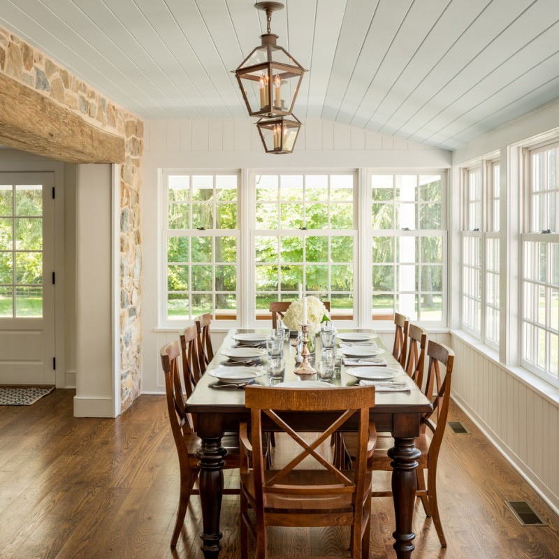 narrow dining room tables hardwood floors tall back chairs multiple windows hanging lamps stone tiles white ceiling farmhouse design