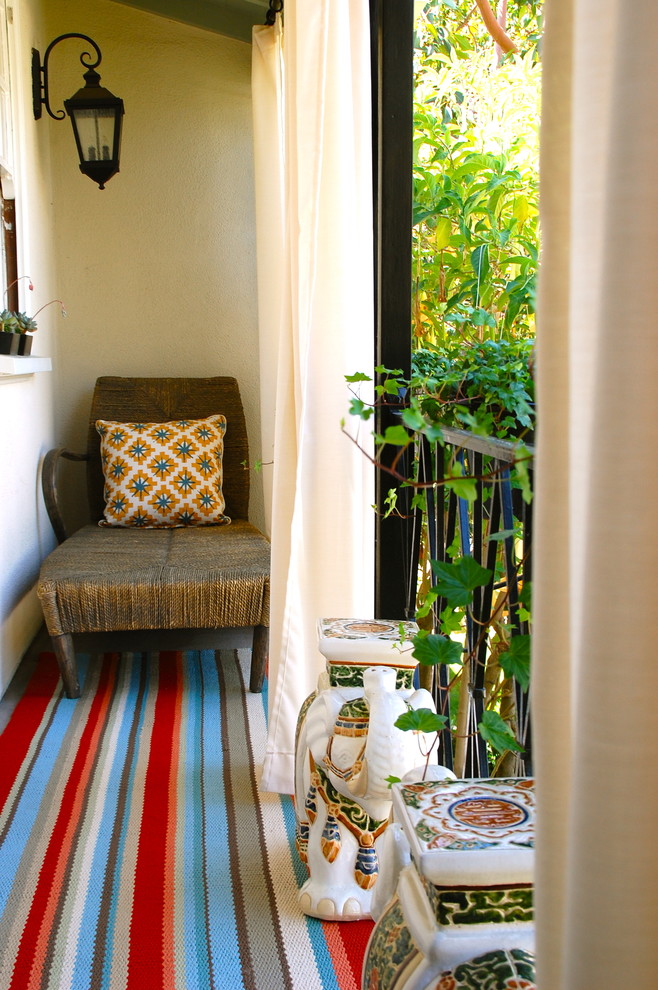 enclosed small balcony with one rattan lounge chair, colorful stripped carpet, china stool, off white curtain