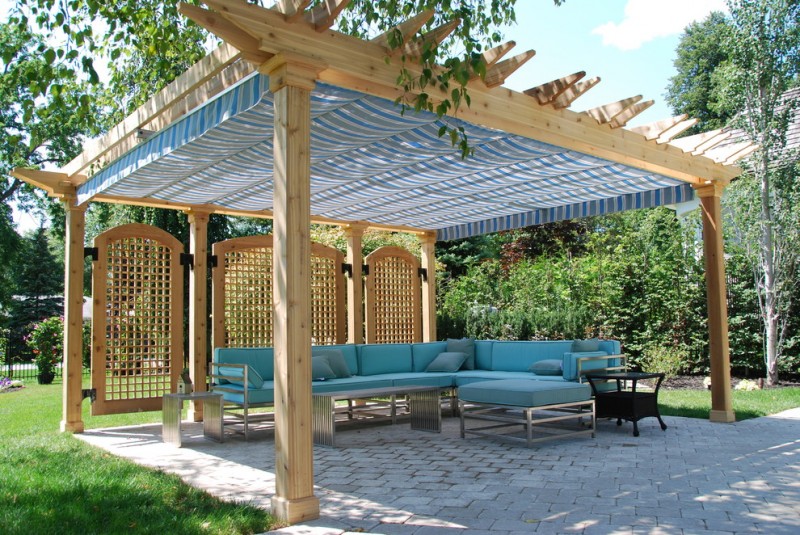traditional backyard patio idea with oak pergola oak partitions L shape blue couch with decorative pillows black side table blue rectractable canopy paver floorings
